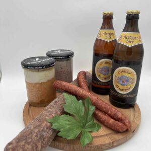Probierpaket Männer Abend, Ahle wurst, knackige Pfefferbeißer, Leberwurst und 2 Metzgerbiere ordentlich auf einem Holzbrett angerichtet für eine deftige Brotzeit.